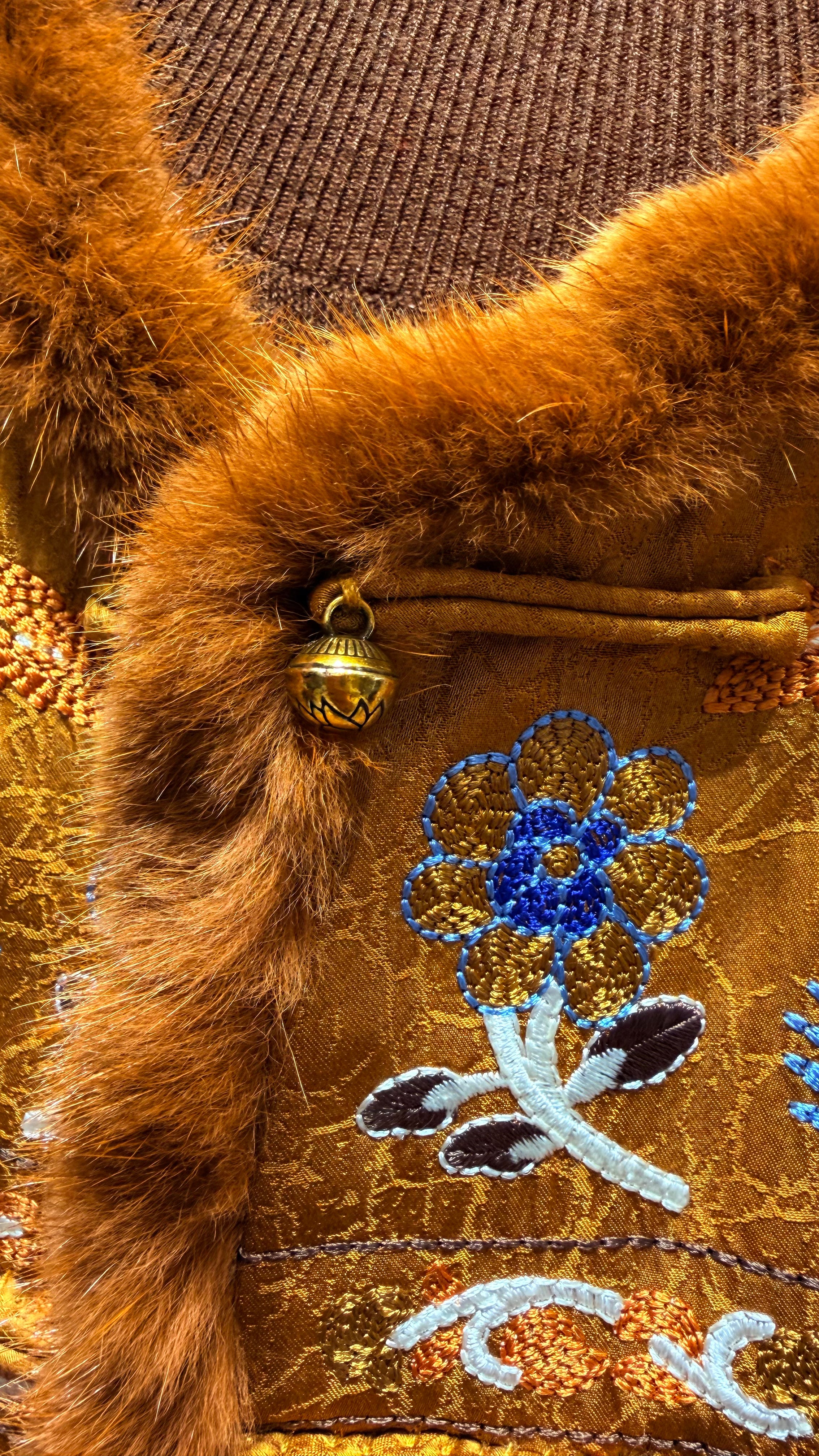 Close-up of a brown textured fabric with embroidered blue flower design and gold bell.