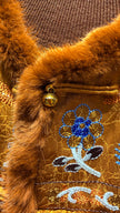 Close-up of a brown textured fabric with embroidered blue flower design and gold bell.