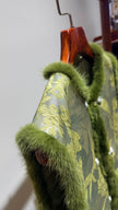 Green floral-patterned garment with fur trim on a wooden hanger against a white wall.
