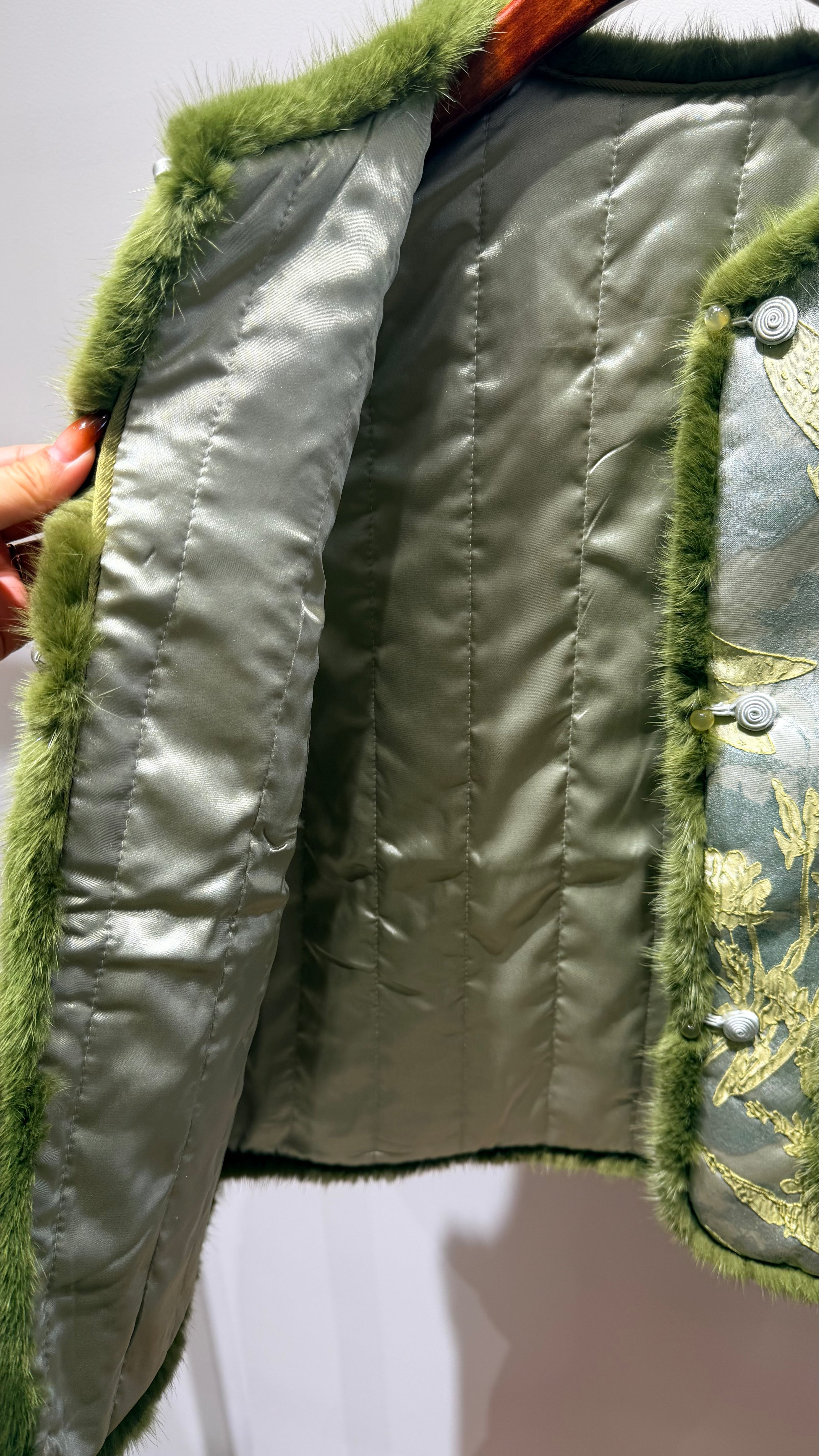 Close-up of a green quilted jacket with fur trim on a white background