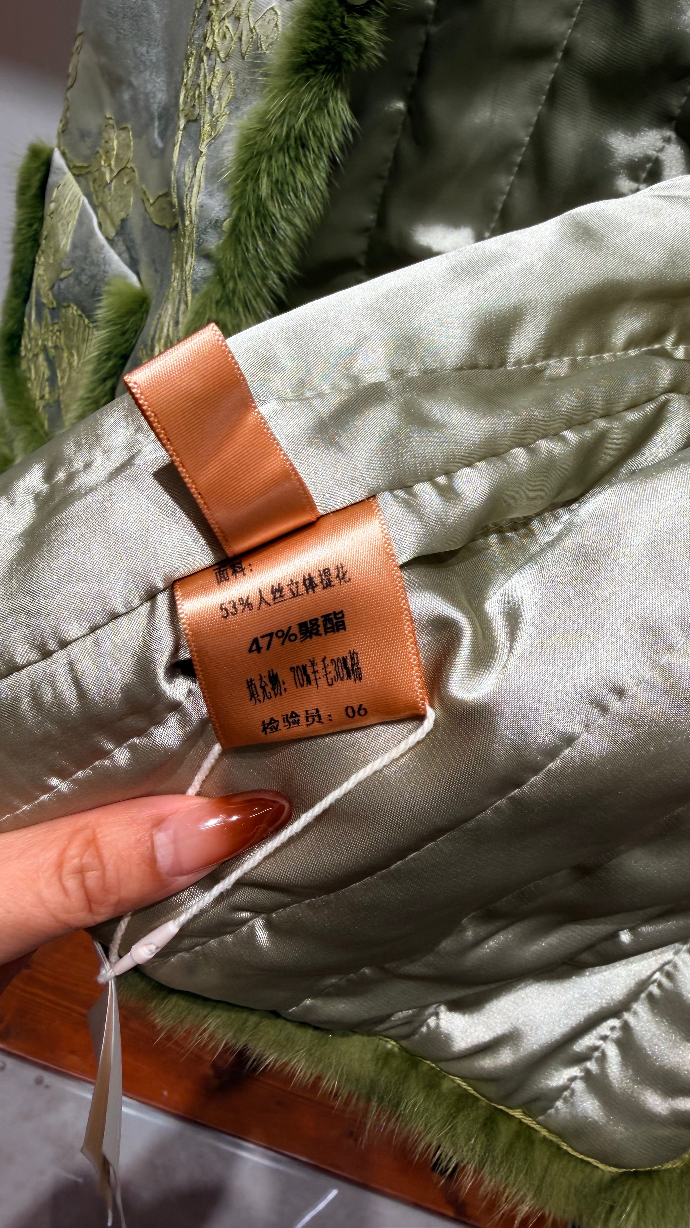 Close-up of a fabric tag on a quilted jacket with a hand holding it.