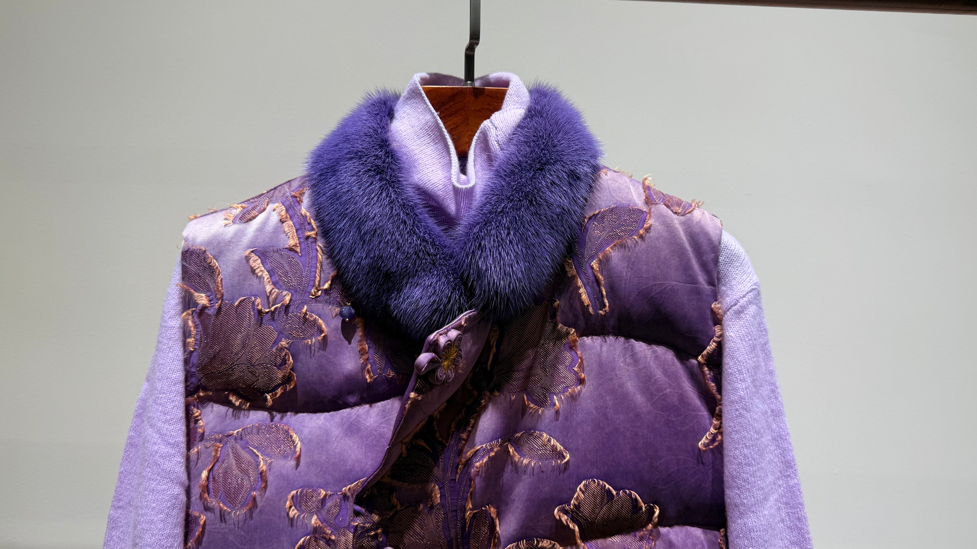 Purple patterned coat with fur collar on a hanger against a light gray background