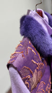 Purple garment with fur trim on a hanger against a light background