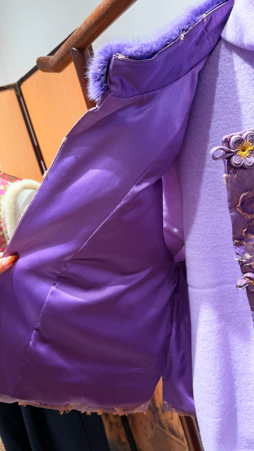 Close-up of a purple garment with a textured surface, possibly a coat or jacket, on a blurred background.
