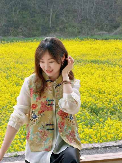 Woman in a colorful embroidered vest sitting in a field of yellow flowers.