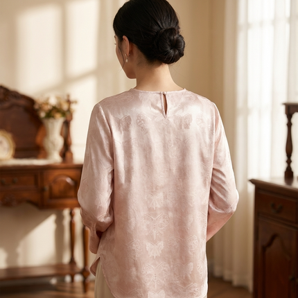  Model in pink blouse back view  standing in a softly lit room with wooden furniture.
