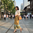 Woman in a gold xiangyunsha skirt walking on a city street with modern buildings and trees in the background